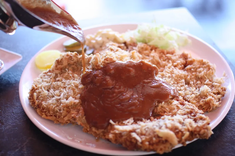 King Katsu Landで衣を付けたカツにソースをかける様子。