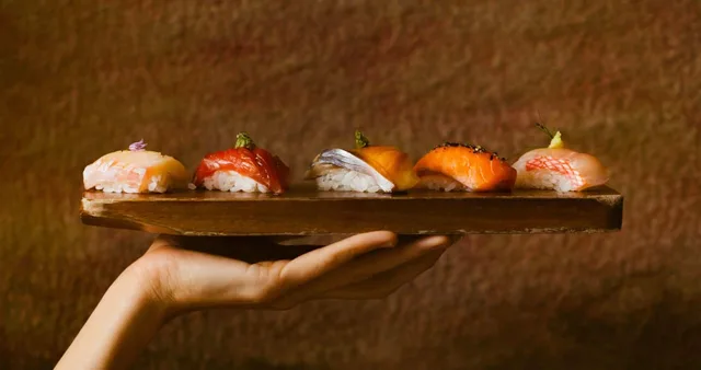 A server holding a wooden board of nigiri at Uchi West Hollywood.